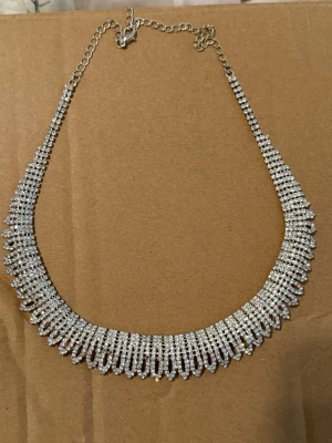 Glittrigt halsband med diamanter  - Snyggt halsband i silverfärg med massor av små glittrande pärlor som ger en lyxig känsla. Halsbandet har ett brett, droppformat mönster och justerbar kedja för perfekt passform. Perfekt för dig som vill sticka ut och addera extra bling till din outfit.