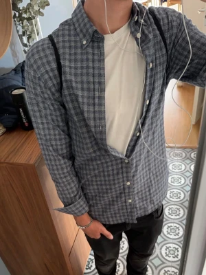 Blårutig skjorta/overshirt från Selected Homme - Säljer en blårutig skjorta med klassisk button-down krage och vita knappar. Skjortan har lång ärm och normal passform, perfekt att bära öppen över en t-shirt. Tillverkad i mjuk bomull för en bekväm känsla.
