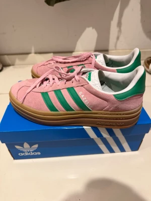 Adidas Gazelle rosa/gröna sneakers - Säljer ett par Adidas Gazelle sneakers i rosa mocka med gröna detaljer. Väldigt fint skick. Storlek 41.5