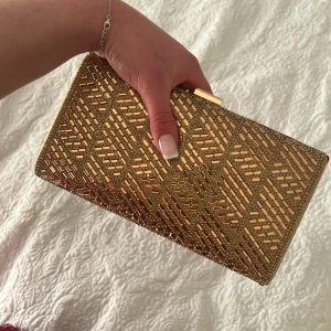 Guldig glittrig väska clutch - Fin väska använd en gång, guld/glittrig. Fin och liten väska. Lång kedja kommer med.
