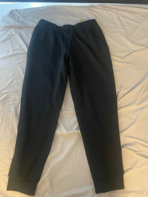 Svarta Nike mjukisbyxor  - Ett par svarta mjukisbyxor med dragsko i midjan och muddar vid bensluten. Byxorna har en avslappnad passform och är tillverkade i ett mjukt och bekvämt material, perfekt för chill dagar. Klassisk design utan synligt märke.