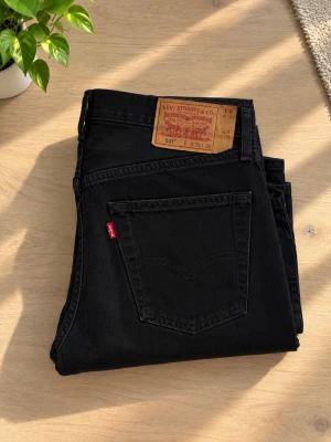Svarta Levi's 501 jeans - Säljer ett par klassiska svarta Levi's 501 jeans med rak passform och fem fickor. Jeansen har den ikoniska läderlappen bak i midjan och röd Levi's-tag på bakfickan. Perfekta för dig som gillar tidlös stil och denim.