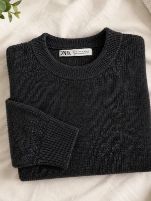 Mörkgrå stickad tröja från ZARA - Snygg mörkgrå stickad tröja från ZARA med rund halsringning och ribbade muddar vid ärmslut och nederkant. Tröjan har en klassisk rak passform och är tillverkad i ett mjukt, grovstickat material som passar perfekt till kyligare dagar.