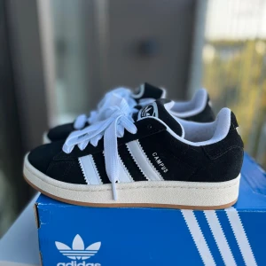 Adidas Campus 00s svarta - Säljer mina Adidas Campus 00s i svart/vitt   Använda endast 1 gång, men fick tyvärr skoskav då mina fötter hade växt och kan därför inte använda dem.   De är i väldigt fint skick och har endast använts en gång. Lite mörk färg från strumpor syns på insidan, se bilder, men inget som påverkar skornas utseende när de används.  Skriv innan du köper då jag har en till annons på denna. Skriv för fler bilder☺️