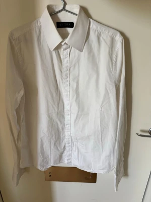 Vit klassisk skjorta från Tiger  - Säljer en stilren vit skjorta från Tiger. Skjortan har klassisk krage, långa ärmar och knäppning framtill. Perfekt för dig som gillar en clean och tidlös look. Tillverkad i bomull för skön känsla och bra passform.(m)