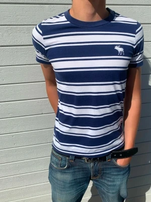 Randig blåvit t-shirt Abercrombie - Snygg randig T-shirt från Abercrombie & Fitch med den klassiska loggan på bröstet. Storlek S och passar true to size. Modellen är 178 och väger 65 kg.  Skriv vid frågor eller funderingar!