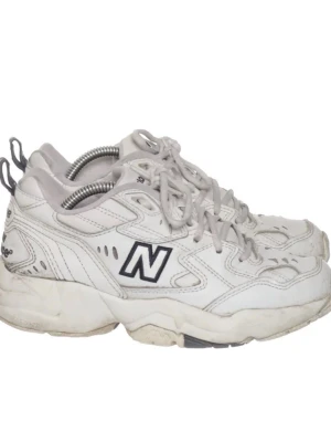 Vita New Balance 608 sneakers - Chunky vita sneakers från New Balance med svart N-logga på sidan. Skorna har tjock sula, vita skosnören och detaljer i grått. Ovandelen är i läder med meshpartier för extra komfort. Skorna är i använt skick i storlek 37