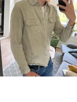 Grön overshirt med slitningar  - Snygg grön overshirt  med två bröstfickor och knappar framtill. Skjortan har klassisk krage och lång ärm, perfekt att styla med jeans för en avslappnad look.Om du har frågar är det bara att fråga på. Pris går att diskutera med seriösa köpare. Kolla in min profil och se om du hittar något mer intressant. Mvh Larsen_Closet