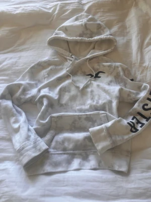 Vit hoodie från Hollister - Snygg vit hoodie från Hollister med tie-dye mönster och svart logga på bröstet, Stor ficka framtill och tryck på ena ärmen☺️