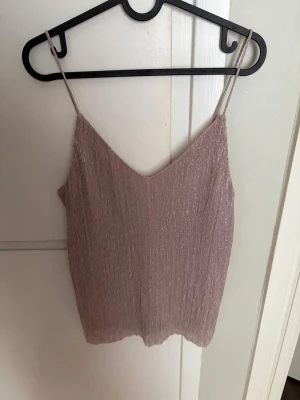 Ljuslila glittrig linnetopp Gina Tricot - Säljer en ljuslila glittrig linnetopp från Gina Tricot med tunna axelband och v-ringad hals. Toppen har en snygg, lätt skimrande yta och är perfekt för att lyfta vilken outfit som helst.