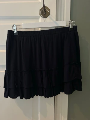 volangkjol från Brandy Melville - Supersöt kortkjol från Brandy Melville med dubbla volanglager och elastisk midja. Kjolen har en flowy passform och är perfekt för dig som gillar en enkel men trendig stil. Materialet känns mjukt och lätt. Den ser svart ut men är marin blå. Det är en one size men skulle säga att den är S. Aldrig använt 