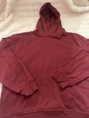 Vinröd hoodie från H&M - Mysig vinröd hoodie från H&M med klassisk huva och känguruficka framtill. Tillverkad i mjukt bomullsmaterial och har ribbade muddar vid ärmslut och nederkant. Perfekt för en avslappnad och chill stil.