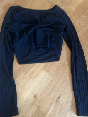 Svart ribbad croppad topp Shein - Säljer en svart croppad topp från Shein med lång ärm och ribbad struktur. Toppen har en snygg omlott-detalj framtill som ger en cool twist till outfiten. Perfekt för dig som gillar trendiga och stilrena plagg.