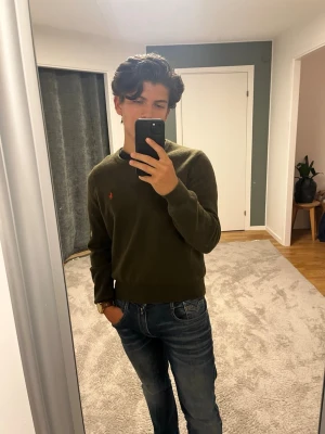 Olivgrön stickad tröja Polo Ralph Lauren - Snygg olivgrön stickad tröja från Polo Ralph Lauren med rund halsringning och den klassiska röda loggan broderad på bröstet. Tröjan har långa ärmar och ribbade muddar vid ärmslut och nederkant. Perfekt till jeans för en avslappnad stil. Tveka inte på att skriva om du har frågor eller funderingar🌟😊