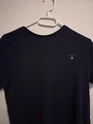 Mörkblå t-shirt från GANT - Snygg mörkblå t-shirt från GANT i regular fit. Klassisk rund halsringning och diskret GANT-logga broderad på bröstet. Tillverkad i mjuk bomull som känns skön mot huden. Perfekt basplagg till garderoben.