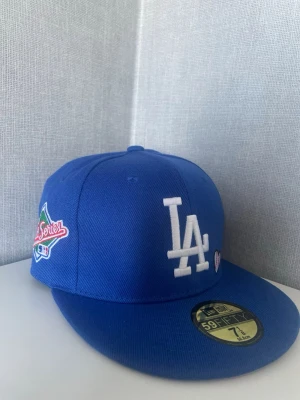 LA BASEBALL lover keps - Snygg blå snapback-keps med LA Dodgers-logga i vitt framtill och broderad patch på sidan. Klassisk rak skärm och broderade detaljer, inklusive ett litet hjärta med basebollmotiv. Perfekt för dig som gillar sportig streetstyle.
