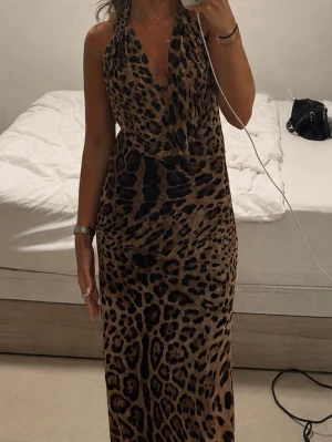 Långklänning med leopardmönster - Snygg långklänning med leopardmönster och halterneck. Klänningen har djup v-ringning och figurnära passform. Har en djup öppen rygg. Klänningen är från design by si och har tyvärr inte kommit till användning då den där för lång. Är 160 cm🥰