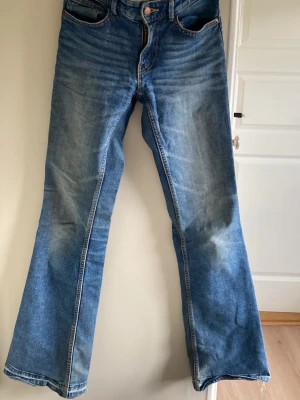 Blå bootcut jeans från Lindex - Säljer ett par blå bootcut jeans från Lindex i modellen Fay. Jeansen har klassisk femficksdesign, normalhög midja och utsvängda ben. Tillverkade i denim med snygga slitningar och kontrastsömmar. Perfekta till sneakers eller boots.