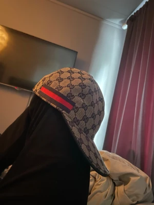 Gucci keps  - Säljer en snygg Gucci keps i beige med klassiskt GG-mönster över hela kepsen. På sidan finns en röd och marinblå rand som ger extra stilpoäng. Kepsen har böjd skärm och är tillverkad i ett slitstarkt tygmaterial. Kan tänkas byta mot någon annan keps