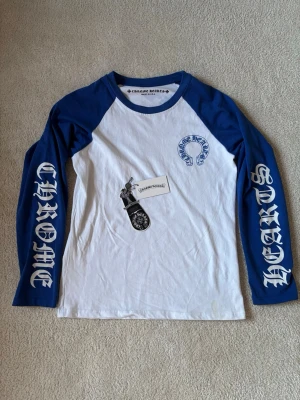 Chrome Hearts långärmad t-shirt blå/vit - Snygg långärmad t-shirt från Chrome Hearts med blå ärmar och vit kropp. Stora tryck på ärmarna och logga på bröstet. Perfekt för dig som gillar streetwear och vill sticka ut med en unik design.