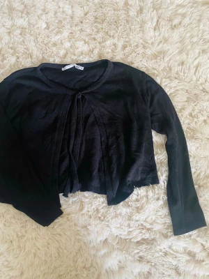 Svart tunn kofta med knytband - Snygg svart tunn kofta med långa ärmar och knytband framtill. Passar perfekt över ett linne eller klänning. Materialet ser ut att vara mjukt och lätt, vilket gör den enkel att styla till olika outfits. Jag säljer den på grund av att jag inte advönder den längre💗