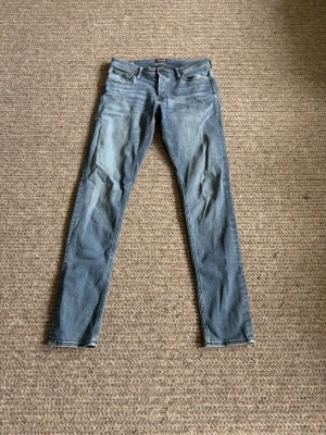 Jeans - Passar 32/34. Snygga blå jeans i slim fit-modell med klassisk femficksdesign och knappgylf. Jeansen har en lätt tvättad look och raka ben. Perfekta till en avslappnad stil och passar till det mesta i garderoben.