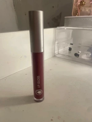 Mörkrosa läppglans med silverlock - Snyggt mörkrosa läppglans i tub med stilrent silverfärgat lock. Tuben är smal och enkel att ta med i väskan. Ger en glansig finish och har en modern look. Perfekt för dig som vill ha färg och glans på läpparna.