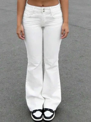 Vita bootcut jeans med låg midja - Snygga vita bootcut jeans med låg midja och dubbla knappar framtill. Jeansen har klassiska fem fickor och är tillverkade i ett stretchigt denimtyg som sitter bekvämt. Perfekta för dig som vill ha en clean och trendig look.