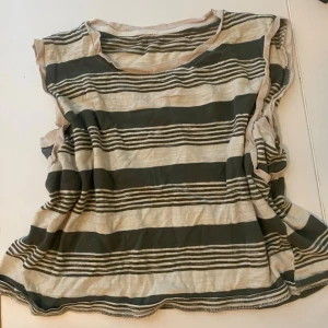 Randig beige och grön linnetopp - Säljer en avslappnad linnetopp med breda och smala ränder i beige och grönt. Toppen är ärmlös och har en rund halsringning. Perfekt för varma dagar och enkel att styla med jeans eller shorts.
