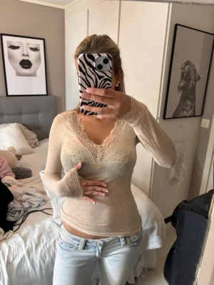 Beige Kashmir Intimissimi tröja med spets - Säljer en beige långärmad intimissimi tröja med v-ringning och fina spetsdetaljer vid halsringning och ärmslut. Toppen är tight i passformen och har en tunn, mjuk känsla som passar perfekt till jeans eller kjol.