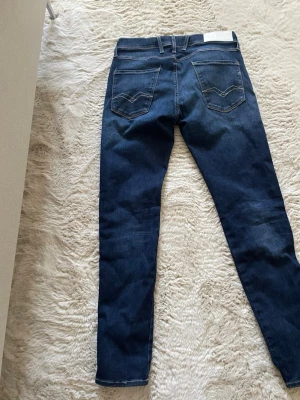 Mörkblå skinny jeans från Replay - Snygga mörkblå skinny jeans från Replay med klassiska fem fickor och kontrastsömmar. Jeansen har en smal passform och är tillverkade i stretchigt denim för extra komfort. Perfekta för en trendig och avslappnad look.