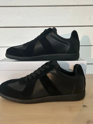 Maison margiela skor  -  Säljer ett par riktigt clean Maison Margiela GAT Triple Black. 🔥 En tidlös sneaker som passar till allt och lyfter vilken outfit som helst.  ✨ Helsvarta (Triple Black) ✨ Stilrena & bekväma ✨ Lättmatchade till alla outfits ✨ Säljs då de inte kommer till användning  📩 Skicka gärna ett meddelande vid frågor eller om du vill ha fler bilder. Först till kvarn! 🚀