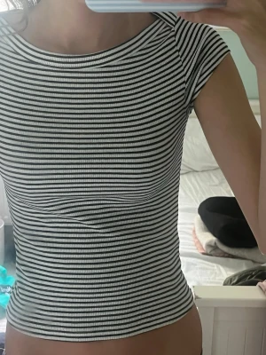 Randig ribbad topp med kort ärm - Säljer en svartvit randig topp med ribbad struktur och korta ärmar. Toppen har en tight passform och rund halsringning. Perfekt att styla med jeans eller kjol för en enkel och snygg look.