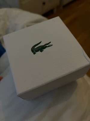 Silverfärgat armband från Lacoste - Snyggt armband i silverfärgad metall från Lacoste. Armbandet har rektangulära länkar med ingraverade detaljer och den klassiska Lacoste-krokodilen på vissa länkar. Kommer i original ask och tygpåse med logga.