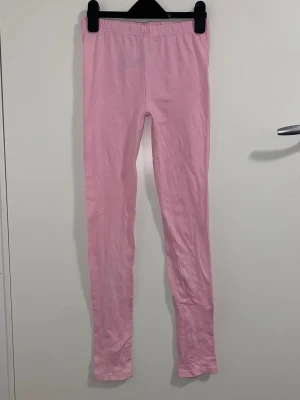 Ljusrosa leggings med resårmidja - Säljer ett par ljusrosa leggings med smal passform och resår i midjan. De är helfärgade och har långa ben. Perfekta att matcha med oversized tröjor eller hoodies. Materialet ser ut att vara mjukt och stretchigt, troligen bomull eller bomullsblandning.