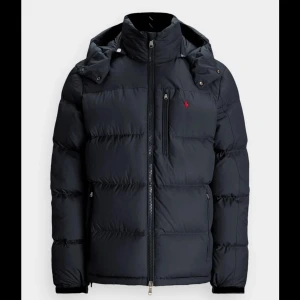 Svart jacka från Polo Ralph Lauren - Skick: 6/10, nypris: 5500kr. Svart jacka från Polo Ralph Lauren med avtagbar huva, dragkedja framtill och röd broderad logga på bröstet. Priset är billigt pågrund av att den har lite små hål. Se defekter på de andra bilderna