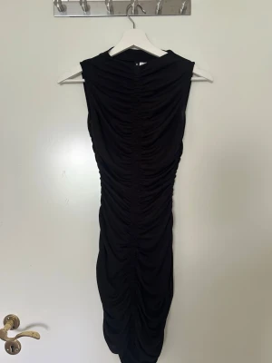Svart långklänning med draperingsdetaljer  - Säljer en svart långklänning med snygga  draperingsdetaljer längs sidorna. Klänningen är ärmlös och har en slim passform som framhäver figuren.