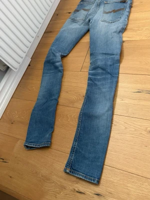 Ljusblå raka jeans med slitningar - Säljer ett par ljusblå jeans med raka ben och diskreta slitningar. Jeansen har klassisk femficksdesign och kontrastsömmar. Materialet är denim i bomull och passformen är avslappnad men ändå smal. Perfekta för en casual look.