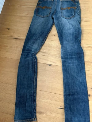 Blå slim fit jeans med broderade fickor - Snygga blå slim fit jeans med slitningar och broderade detaljer på bakfickorna. Klassisk femficksmodell med dragkedja och knapp. Jeansen har en tvättad look och raka ben, perfekta till vardagsstilen.