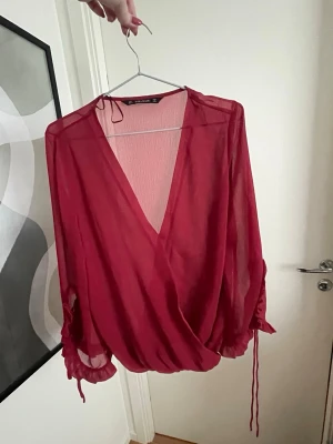 Röd blus  - Vinröd elegant omlottblus i transparent material med djup V-ringning och långa ärmar. Ärmarna har dragsko och volangdetaljer vid ärmslut. Från Zara i storlek L