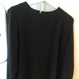 Svart klänning med dragkedja - Elegant svart blus med långärmad design och dragkedja i ryggen. Perfekt för en stilren look.