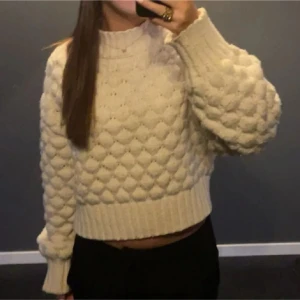 Beige stickad tröja - Säljer en mysig beige stickad tröja med ett unikt bubbligt mönster. Tröjan är croppad och har långa ärmar med ribbade muddar. Perfekt för kyliga dagar!