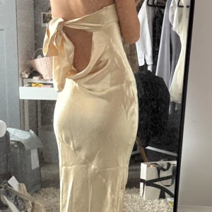 Champagnefärgad/guld axelbandslös klänning med rosett - Säljer min fina guld/champangefärgad balklänning med öppen rygg och rosett bak då jag har köpt en ny! Aldrig använd endast testad, har dock lite trådar som har gått upp i tyget men inget man tänker på eller ser när man har på sig den. Storlek xxs men är justerbar så passar fler storlekar. Köpt för 800 + 250 i tull, helt slutsåld. Kan skicka fler bilder från hemsidan om det behövs