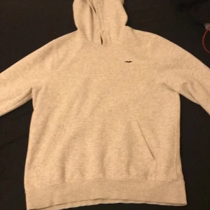 Grå hoodie från Hampton Republic - Säljer en stilren grå hoodie från Hampton Republic. Den har en klassisk design med en liten logga på bröstet och en praktisk ficka framtill. Perfekt för en avslappnad stil.