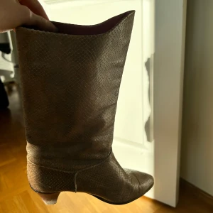 Bruna boots med ormskinnsmönster - Snygga bruna boots med ett ormskinnsmönster. De har en spetsig tå och en låg klack, vilket ger en stilren look. Klacken är ganska sliten. Skriv gärna vid frågor!💕