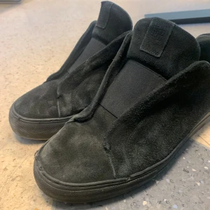 Söker byten och säljes  - Snygga svarta sneakers från Axel Arigato i mocka. De har en stilren design med elastiska band över foten istället för traditionell snörning. Perfekta för en minimalistisk look.(tvätt kan lösas)
