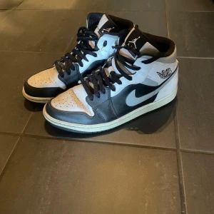 Nike Air Jordans i svart och vit - Snygga Nike Air Jordans i klassisk svart och vit färgkombination. Skorna har en hög modell med snörning och den ikoniska Air Jordan-loggan på sidan. Perfekta för både stil och komfort.