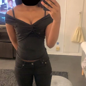 Svart offshoulder topp - Snygg svart offshoulder topp med knytdetalj framtill. Perfekt för en kväll ute eller en speciell tillställning. Toppen har en tight passform som framhäver figuren.