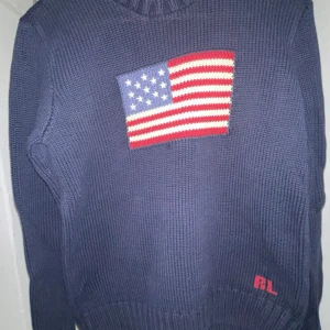 Mörkblå stickad tröja från Polo Ralph Lauren - Pris kan diskuteras ( byter inte )Säljer en mörkblå stickad tröja från Polo Ralph Lauren med en amerikansk flagga på framsidan. Tröjan har långa ärmar och en ribbad krage. Perfekt för en stilren och avslappnad look.