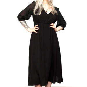 Svart klänning från Disturbia - Elegant svart klänning från Disturbia med trekvartsärmar och v-ringad design. Klänningen har en smockdetalj vid midjan och ett vackert spetsmönster vid halsen. Perfekt för en stilfull look.